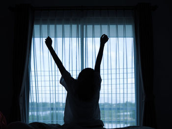 Rear view of woman stretching against window at home