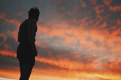 Low angle view of man standing against cloudy sky during sunset