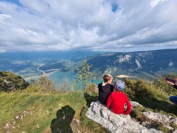 Woman sitting on rock looking at mountains against sky