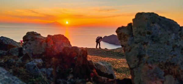 Man standing on rock by sea against sky during sunset