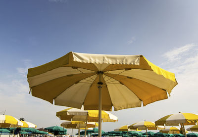 Low angle view of yellow parasols against blue sky during sunny day