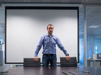 Businessman looking away while standing against projection screen in board room