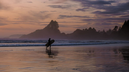 Silhouette woman walking on beach against sky during sunset