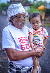 Grandfather carrying son on footpath