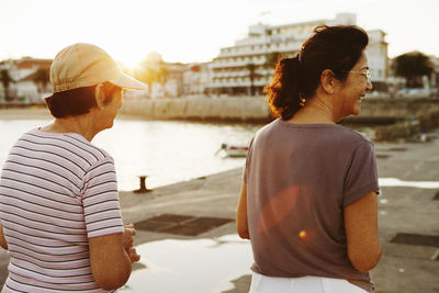 Siblings standing at harbor against city during sunset