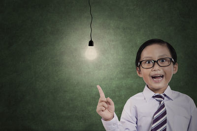 Portrait of boy looking at light bulbs while standing against wall