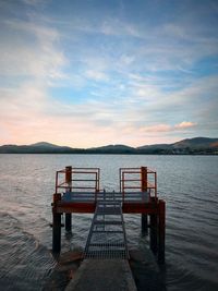 Empty deck chairs by sea against sky