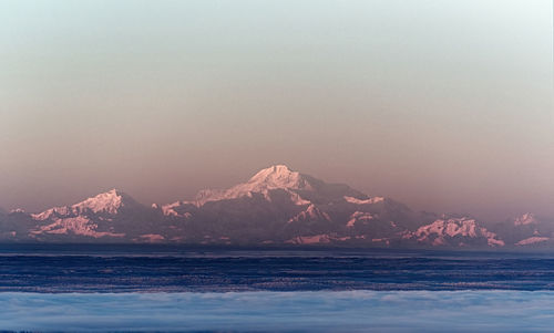 Scenic view of sea by mountain against sky during sunset