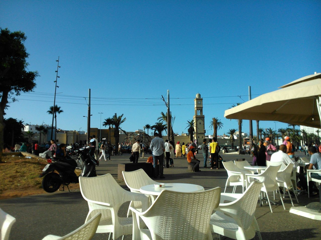 large group of people, clear sky, person, men, leisure activity, sunlight, lifestyles, chair, relaxation, blue, crowd, parasol, shadow, table, sunshade, copy space, sitting, vacations, sunny