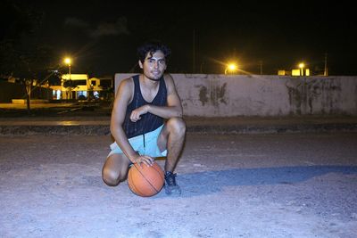 Full length portrait of young man with basketball on street at night
