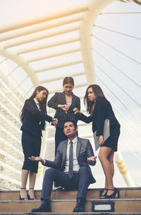 Colleagues showing thumbs down to thoughtful businessman sitting on steps