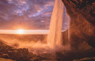 Scenic view of waterfall against sky during sunset