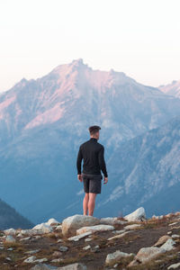 Rear view of man standing on rock in mountains against sky