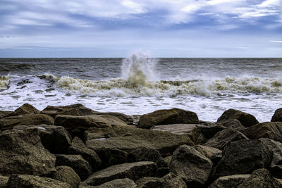 Waves splashing on rocks at shore against sky