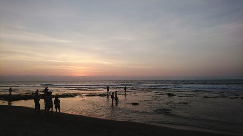 Silhouette people on beach against sky during sunset