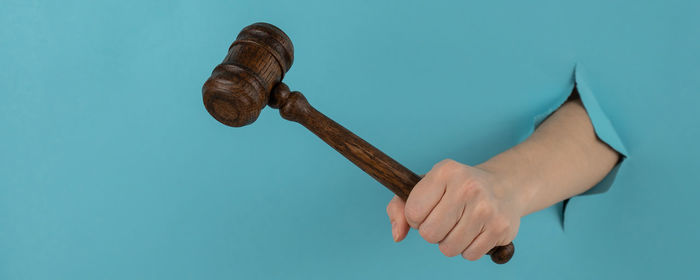 Cropped hand of man holding hammer against blue background