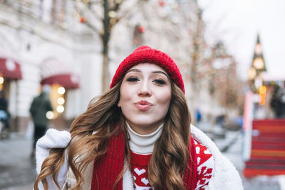Young happy woman with dark curly hair in red knitted hat at the christmas fair in winter street 