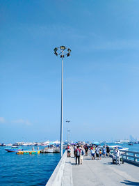 People on street by sea against clear blue sky