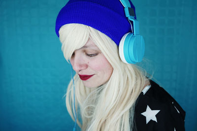 Close-up of woman with blond hair listening music against blue wall