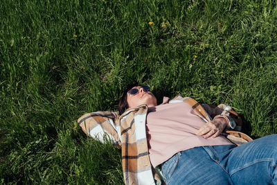 Woman in sunglasses lies on the fresh grass covering her face from the sun with her hand. 