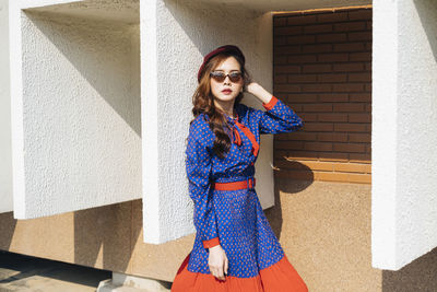 Portrait of young woman standing against building