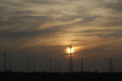 Silhouette wind turbines on field against sky during sunset