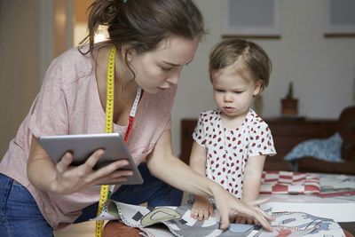 Fashion designer with digital tablet looking at fabric while standing by daughter