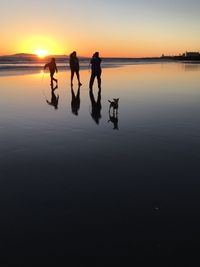 Silhouette people walking on beach against sky during sunset