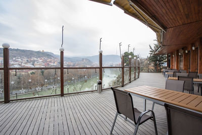 Empty chairs and tables in balcony against sky
