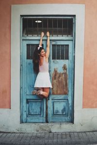 Rear view of cheerful woman hanging on security bars against old blue door