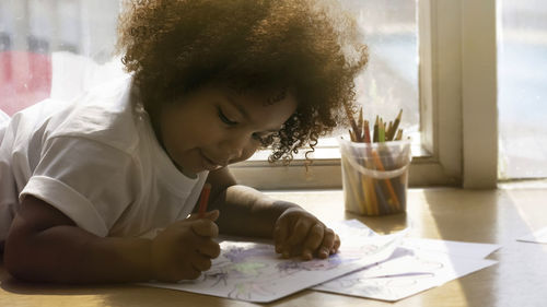 Cute girl drawing in paper while lying on floor at home