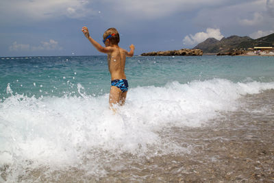 Full length of shirtless man in sea against sky