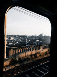 Railroad tracks by buildings against sky seen through train window