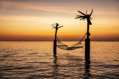 Silhouette tree by sea against sky during sunset