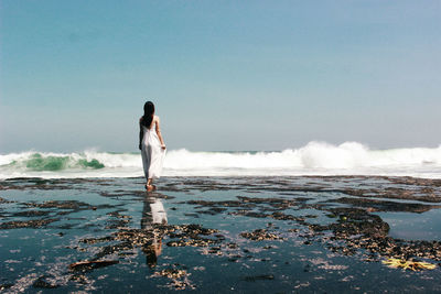 Rear view of woman standing at beach against sky