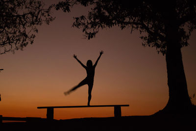 Silhouette man with arms raised against sky during sunset