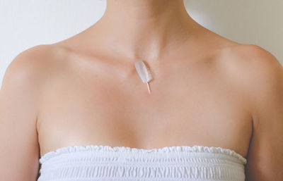 Midsection of woman wearing strapless top with feather on neck against white wall