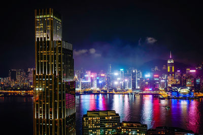 Illuminated buildings by river against sky at night