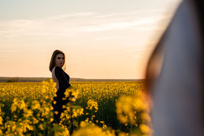 Young woman standing on field against sky during sunset