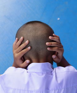 Rear view of boy covering ears against blue wall