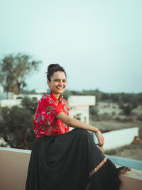 Portrait of smiling young woman standing against sky