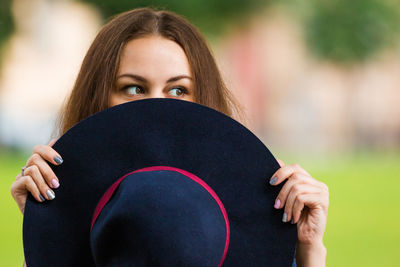 Woman looking sideways while covering face with hat outdoors