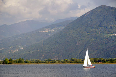 Sailboat sailing on sea by mountains against sky