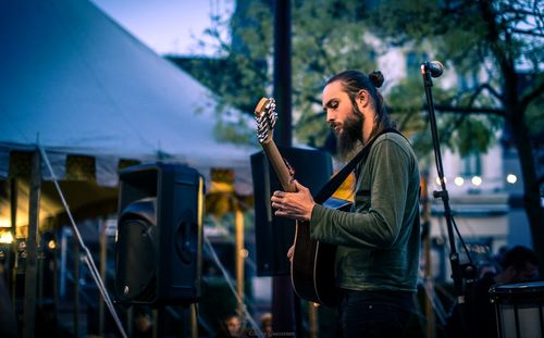 Side view of musician playing guitar on stage during dusk