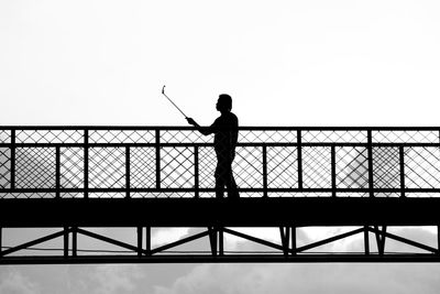 Silhouette of man taking selfie while standing at footbridge