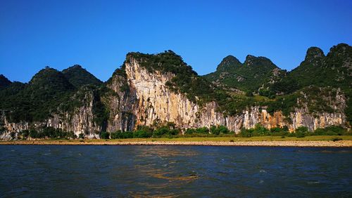 Scenic view of sea and mountains against clear blue sky