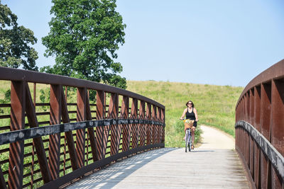 Mature woman riding bicycle on footbridge against clear sky