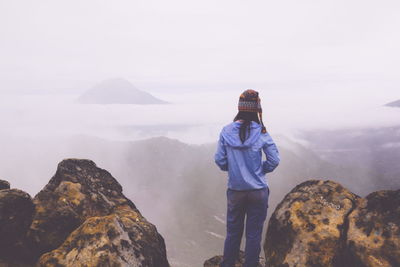 Rear view of woman standing on rock against sky