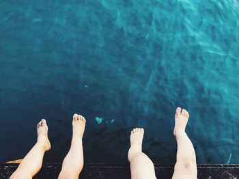 Low section of kids feet dangling over sea