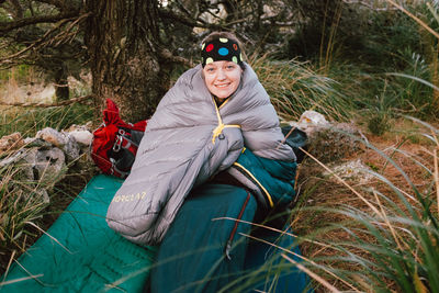 Portrait of smiling young woman sitting in sleeping bag on land